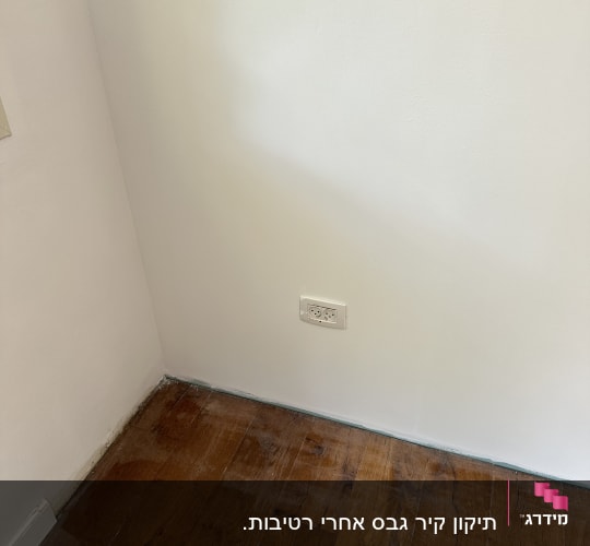 רצפת עץ עם שקע חשמל על קיר לבן